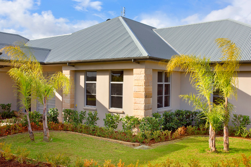 Cette image montre une grande façade de maison beige rustique de plain-pied avec un toit à quatre pans et un toit en métal.