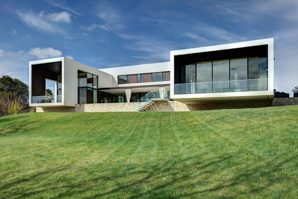 Пример оригинального дизайна: большой, двухэтажный, стеклянный, белый дом в стиле модернизм с плоской крышей