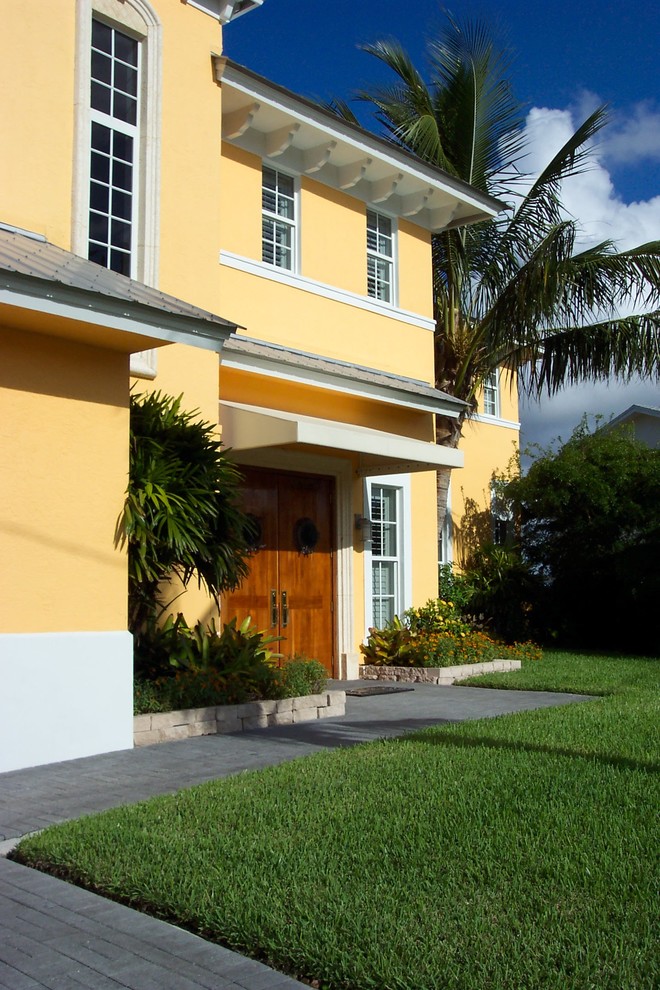 Immagine della villa grande gialla tropicale a due piani con rivestimento in stucco, falda a timpano e copertura in metallo o lamiera
