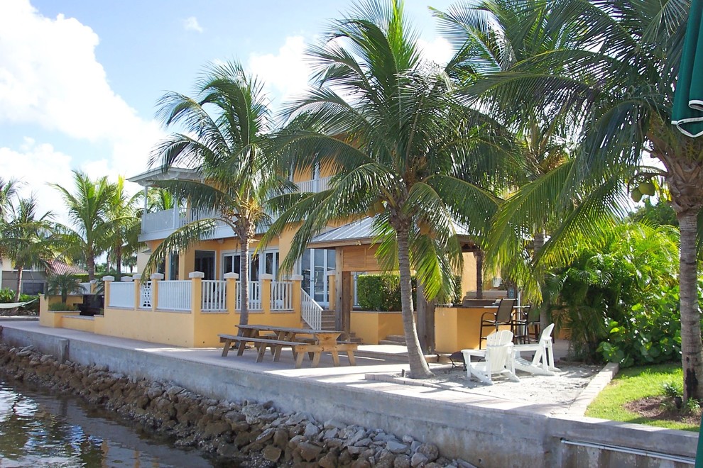 マイアミにあるラグジュアリーなトロピカルスタイルのおしゃれな家の外観 (漆喰サイディング、黄色い外壁) の写真