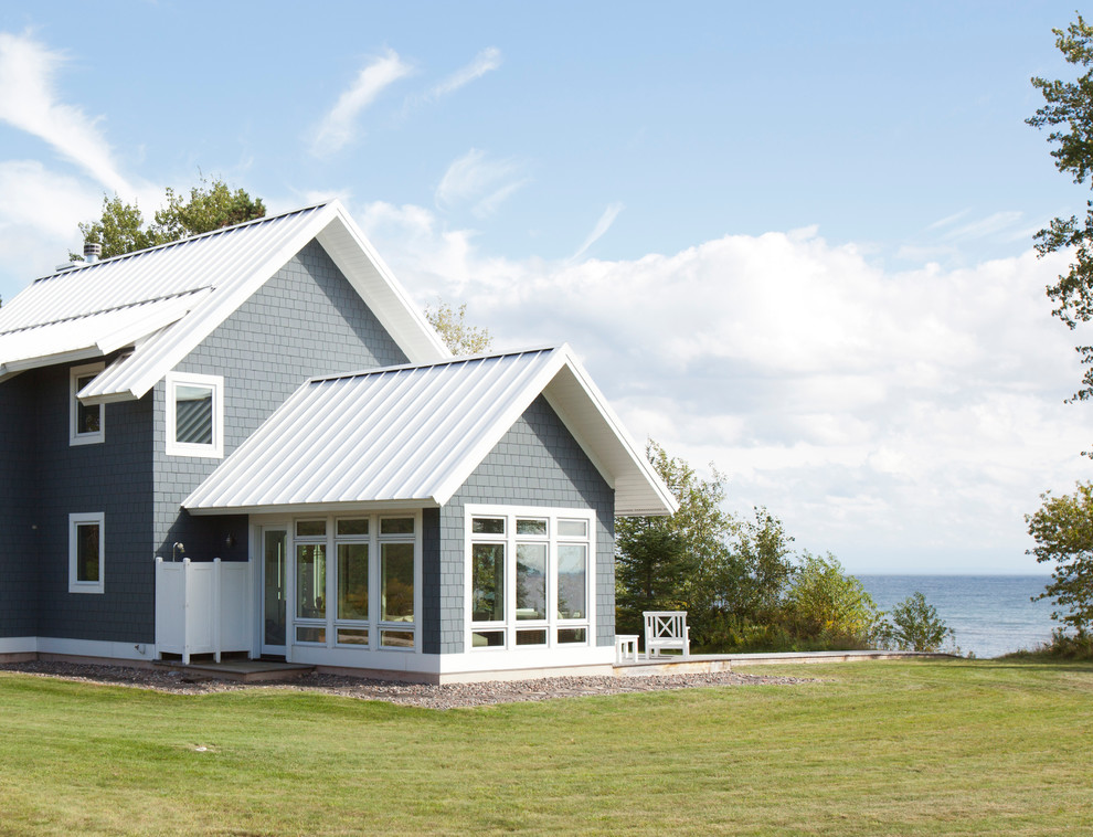 Cette photo montre une petite façade de maison grise bord de mer en panneau de béton fibré à un étage avec un toit à deux pans et un toit en métal.