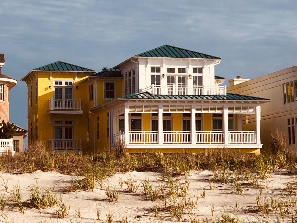 Стильный дизайн: большой, трехэтажный, желтый частный загородный дом в морском стиле с облицовкой из ЦСП, вальмовой крышей и металлической крышей - последний тренд