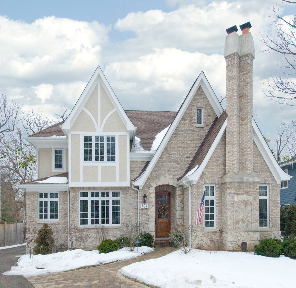 Esempio della facciata di una casa grande beige country a due piani con rivestimento in mattoni e tetto a capanna
