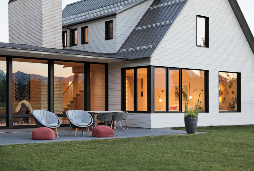 Réalisation d'une façade de maison blanche champêtre en bois de taille moyenne et à un étage avec un toit à deux pans et un toit en métal.