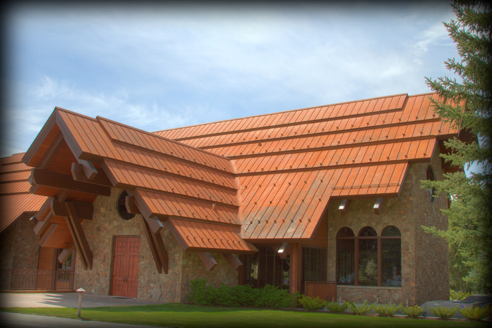 Large rustic brown one-story stone exterior home idea in Other with a hip roof and a metal roof