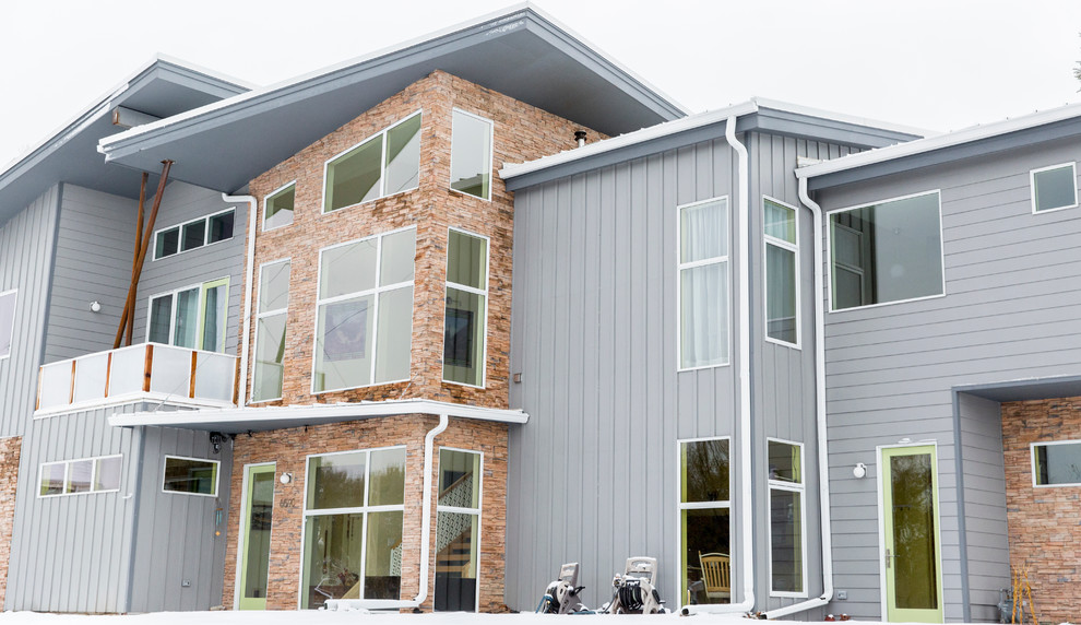 Cette photo montre une façade de maison grise moderne de taille moyenne et à un étage avec un revêtement en vinyle, un toit plat et un toit en métal.