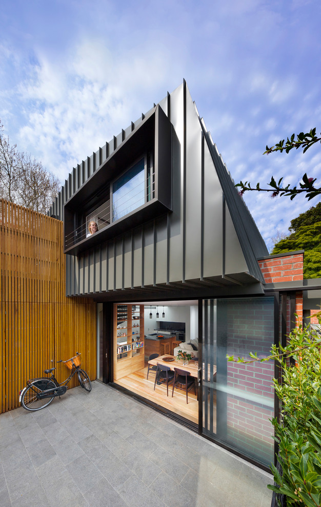 Modelo de fachada de casa gris actual de tamaño medio de dos plantas con revestimiento de metal, tejado a dos aguas y tejado de metal