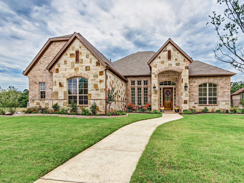 Large traditional brown one-story brick house exterior idea in Dallas with a clipped gable roof and a shingle roof