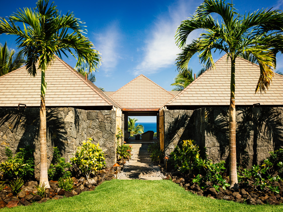 Foto della facciata di una casa tropicale a un piano con rivestimento in pietra e tetto a padiglione
