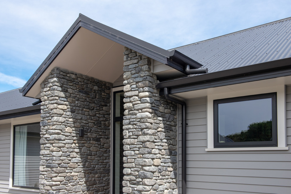 Large trendy gray one-story concrete fiberboard exterior home photo in Christchurch with a hip roof and a metal roof