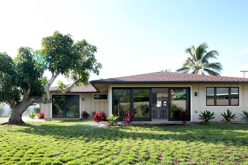 Beige and small world-inspired bungalow house exterior in Hawaii with wood cladding and a hip roof.