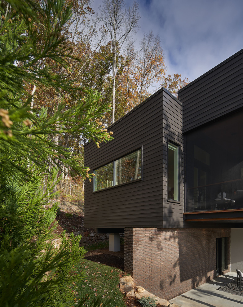 На фото: большой, двухэтажный, черный частный загородный дом в стиле модернизм с комбинированной облицовкой и плоской крышей