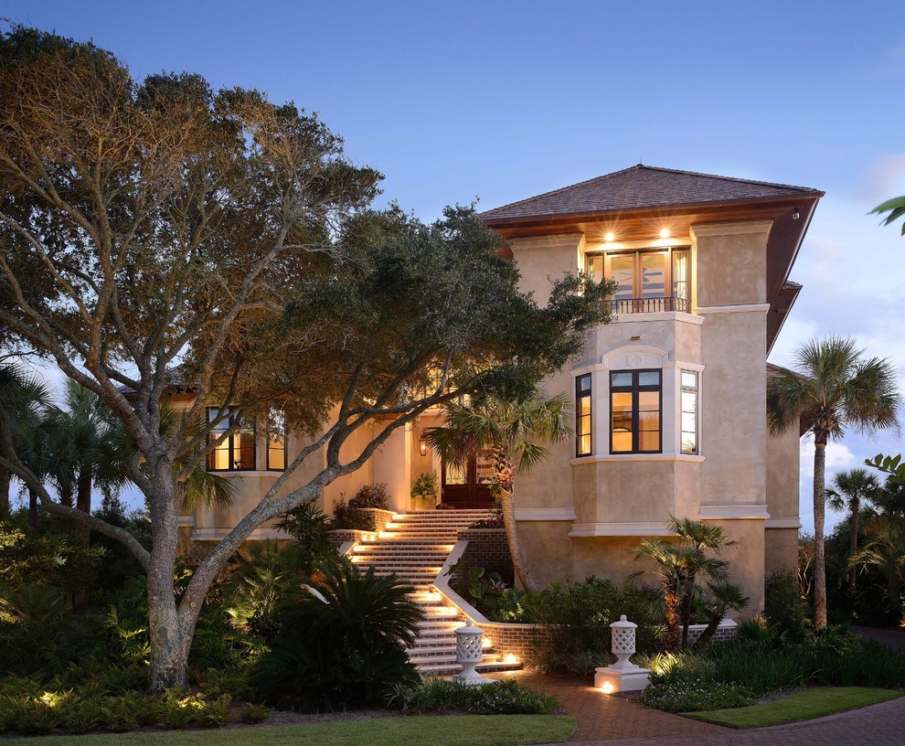 Стильный дизайн: бежевый, большой, двухэтажный дом в средиземноморском стиле с двускатной крышей и облицовкой из цементной штукатурки - последний тренд