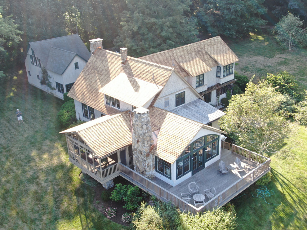 Esempio della villa grande beige country a tre piani con rivestimento in legno, tetto a capanna e copertura a scandole