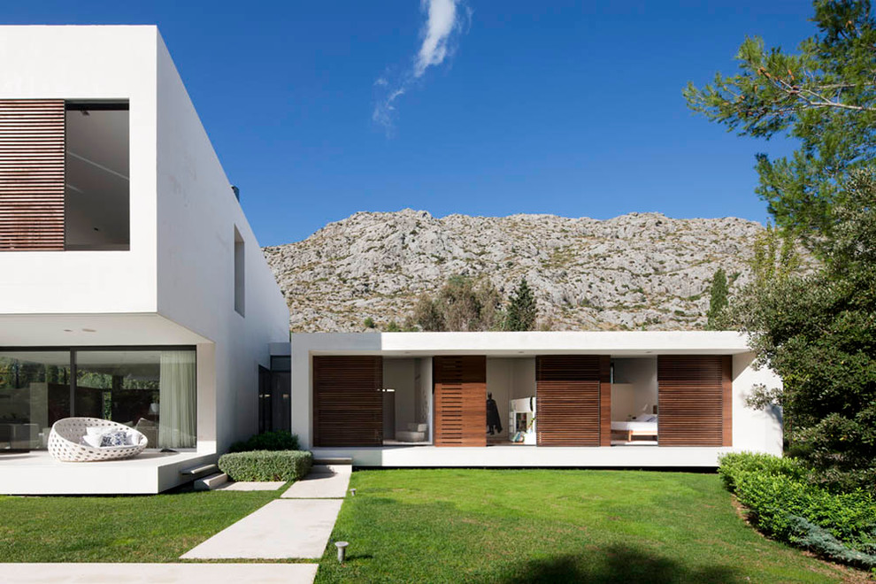 Пример оригинального дизайна: большой, белый дом в стиле модернизм с разными уровнями, облицовкой из цементной штукатурки и плоской крышей