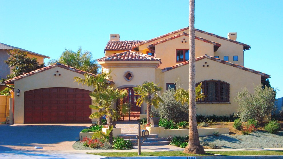 Exemple d'une grande façade de maison beige méditerranéenne en stuc à un étage avec un toit à deux pans et un toit en tuile.