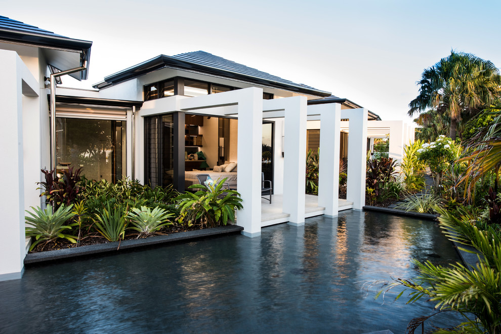 Ejemplo de fachada blanca tropical extra grande de dos plantas con revestimiento de vidrio y tejado a cuatro aguas