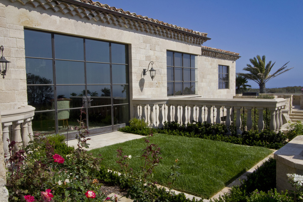 Aménagement d'une grande façade de maison beige méditerranéenne en pierre avec un toit à quatre pans.