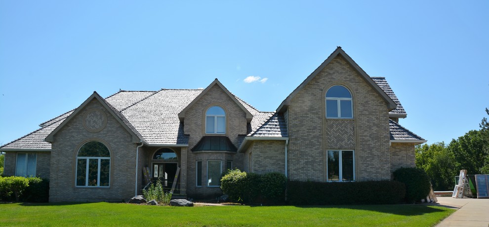 Imagen de fachada de casa beige clásica grande de dos plantas con revestimiento de ladrillo, tejado a dos aguas y tejado de teja de madera