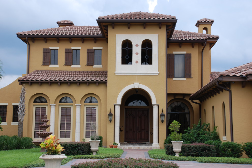 This is an example of an expansive and yellow mediterranean two floor render house exterior in Orlando with a pitched roof.