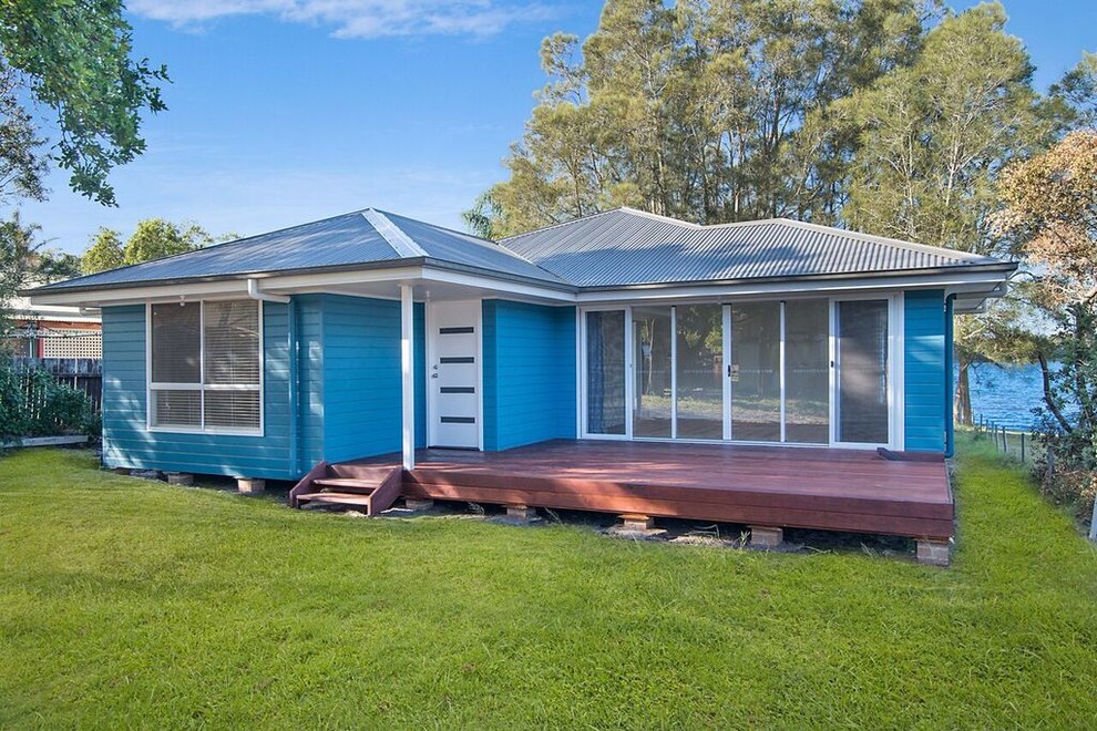 На фото: маленький, одноэтажный, синий дом в морском стиле с облицовкой из ЦСП и вальмовой крышей для на участке и в саду