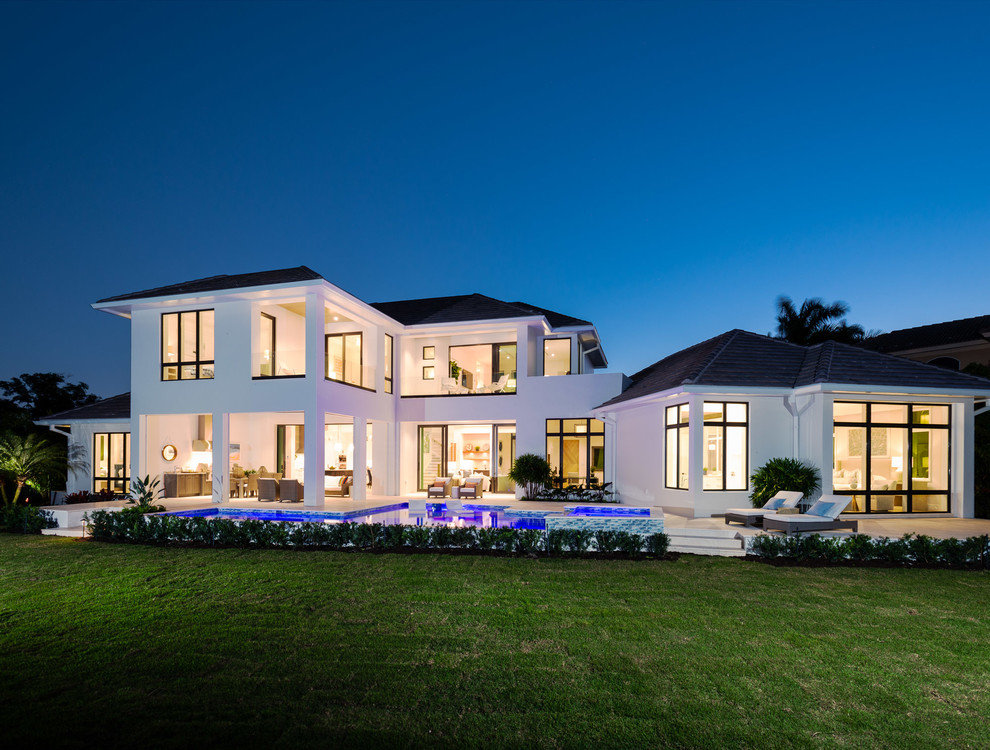 Large beach style white two-story stucco house exterior photo in Miami with a hip roof and a tile roof