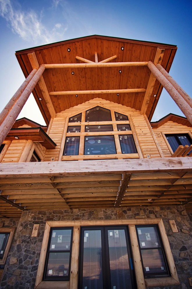 Esempio della villa ampia marrone rustica a due piani con rivestimento in legno, tetto a capanna e copertura a scandole