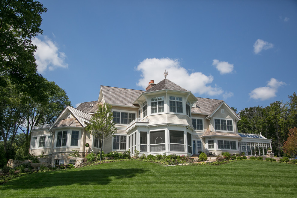 Immagine della villa grande beige classica a due piani con tetto a capanna e copertura a scandole