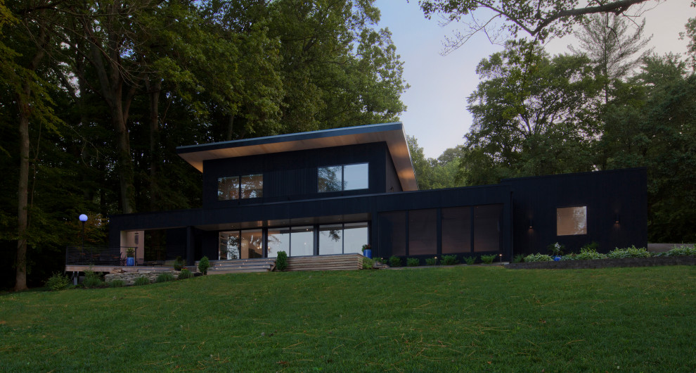 Modelo de fachada de casa negra minimalista de tamaño medio de dos plantas con revestimiento de madera, tejado de un solo tendido y tejado de metal
