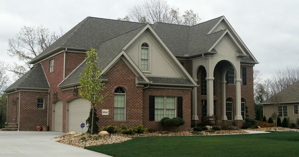 Large traditional beige two-story brick exterior home idea in Other with a shed roof
