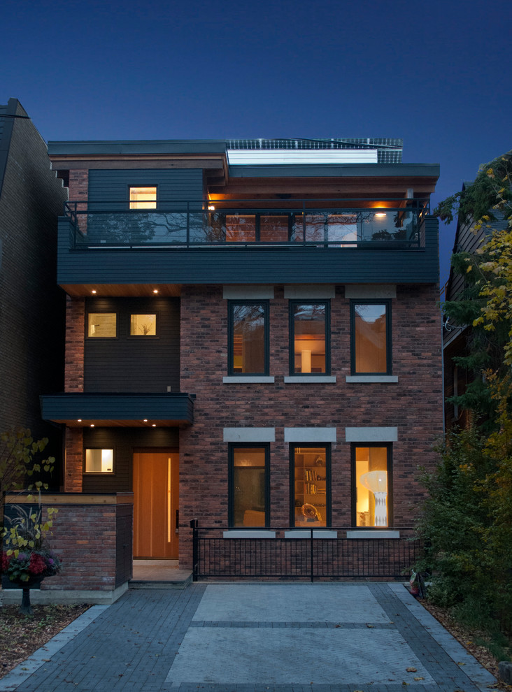 This is an example of a medium sized eclectic brick house exterior in Toronto with three floors and a flat roof.