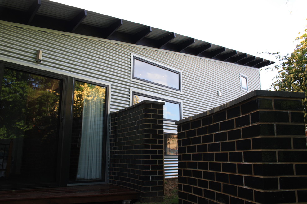 Источник вдохновения для домашнего уюта: маленький, одноэтажный, серый частный загородный дом в современном стиле с облицовкой из металла, плоской крышей и металлической крышей для на участке и в саду