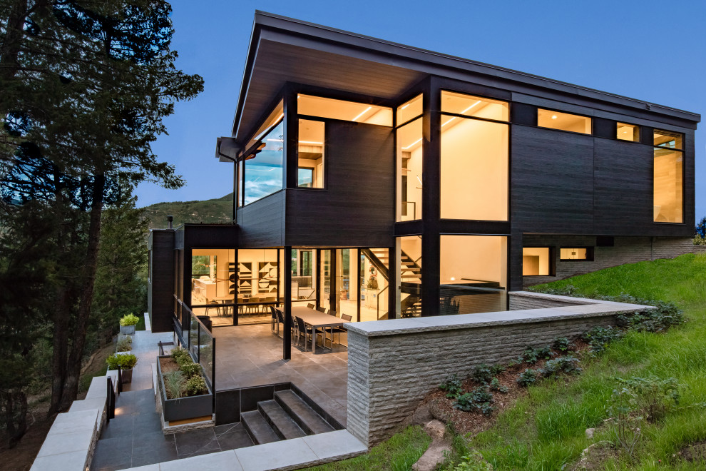 Foto på ett stort funkis brunt hus, med tre eller fler plan, glasfasad, pulpettak och levande tak