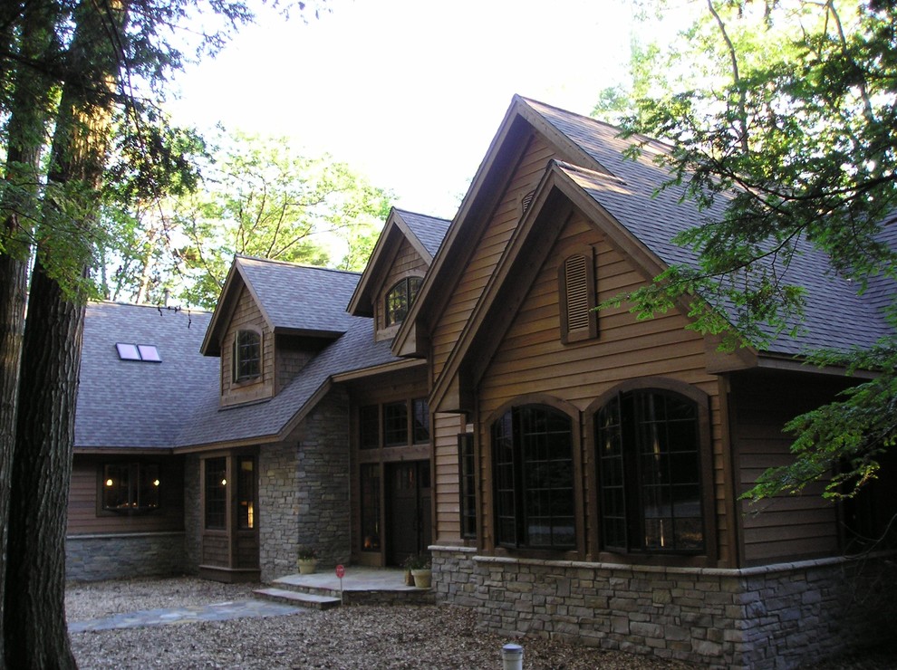 Large and brown rustic bungalow detached house in Other with stone cladding, a hip roof and a shingle roof.