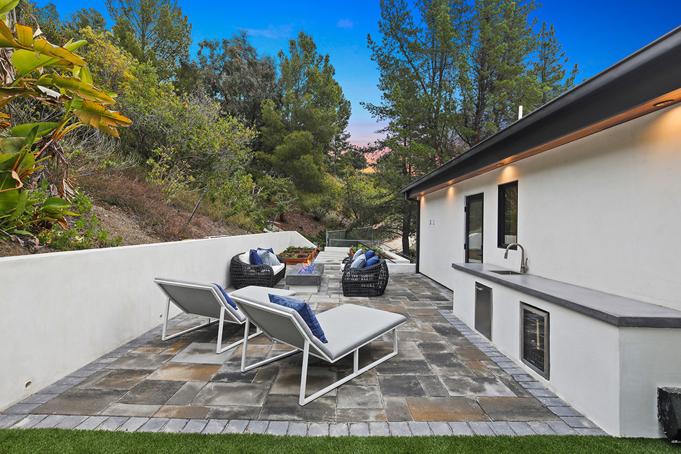 Design ideas for a large modern back patio in Los Angeles with a fire feature, an outdoor kitchen, natural stone paving and no cover.