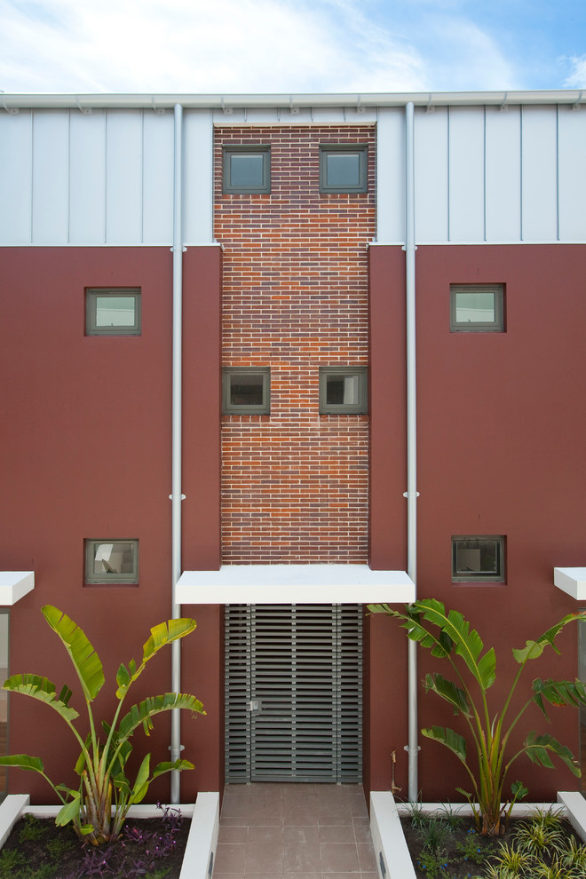 Ejemplo de fachada roja actual grande de tres plantas con revestimientos combinados y tejado plano