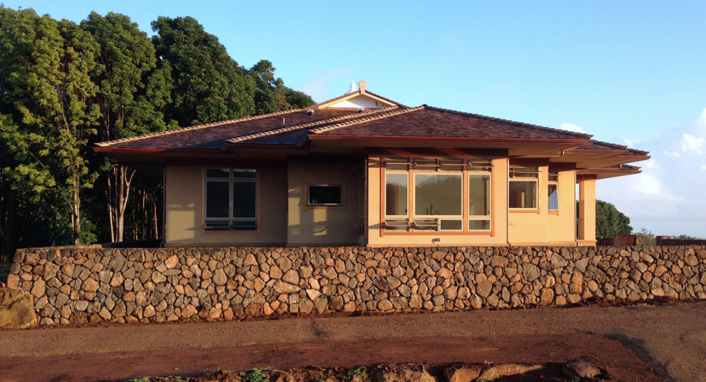 This is an example of a large and beige world-inspired bungalow render detached house in Hawaii with a hip roof and a tiled roof.