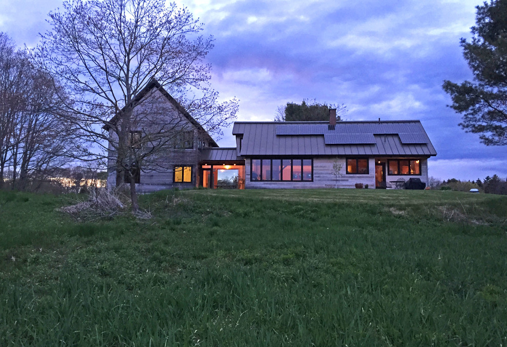 Aménagement d'une grande façade de maison grise campagne en bois à un étage avec un toit à deux pans et un toit en métal.