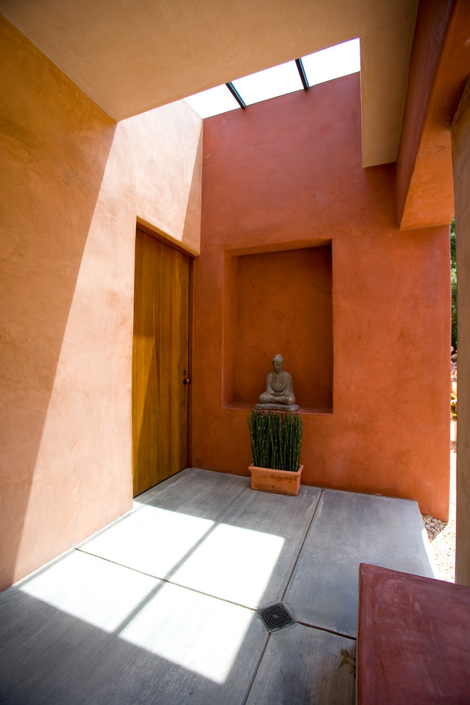Geräumiger Mediterraner Eingang mit oranger Wandfarbe, Betonboden, Einzeltür, hellbrauner Holzhaustür, grauem Boden und gewölbter Decke in Los Angeles