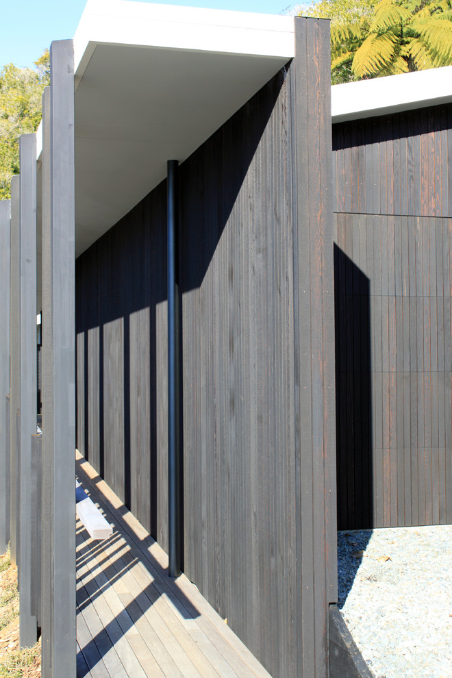 Modelo de fachada negra minimalista grande a niveles con revestimiento de madera y tejado plano