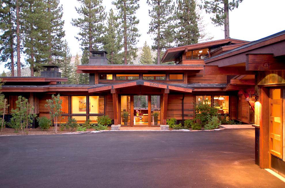 Réalisation d'une grande façade de maison marron chalet en bois à un étage avec un toit à deux pans et un toit en métal.
