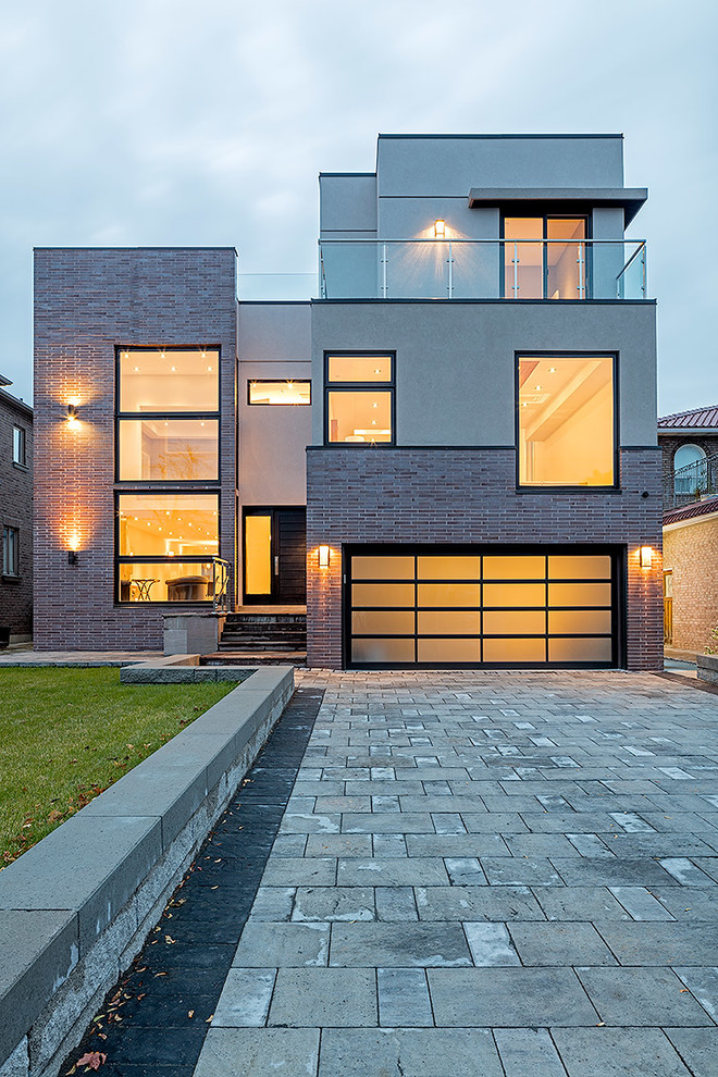 This is an example of a contemporary split-level house exterior in Toronto with a flat roof and mixed cladding.