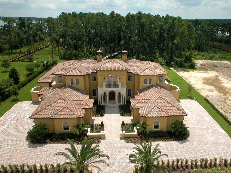 This is an example of a large and yellow mediterranean two floor render detached house in Orlando with a hip roof and a tiled roof.