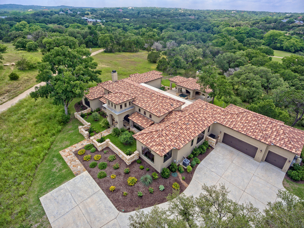 Example of a large tuscan beige two-story stucco exterior home design in Austin with a hip roof