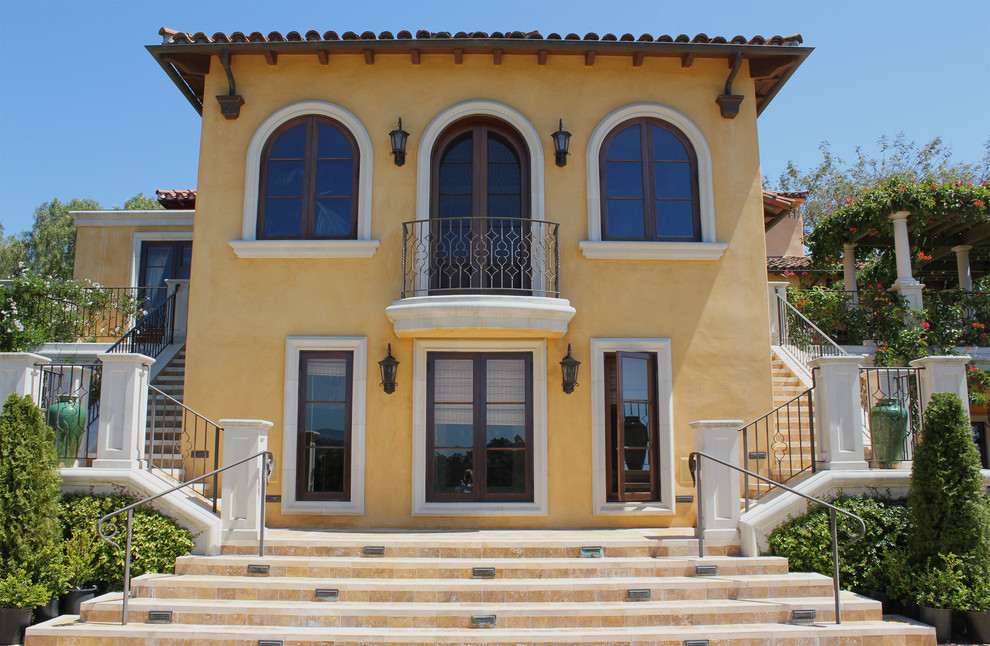 Diseño de fachada de casa amarilla mediterránea grande de dos plantas con tejado a cuatro aguas y tejado de teja de barro