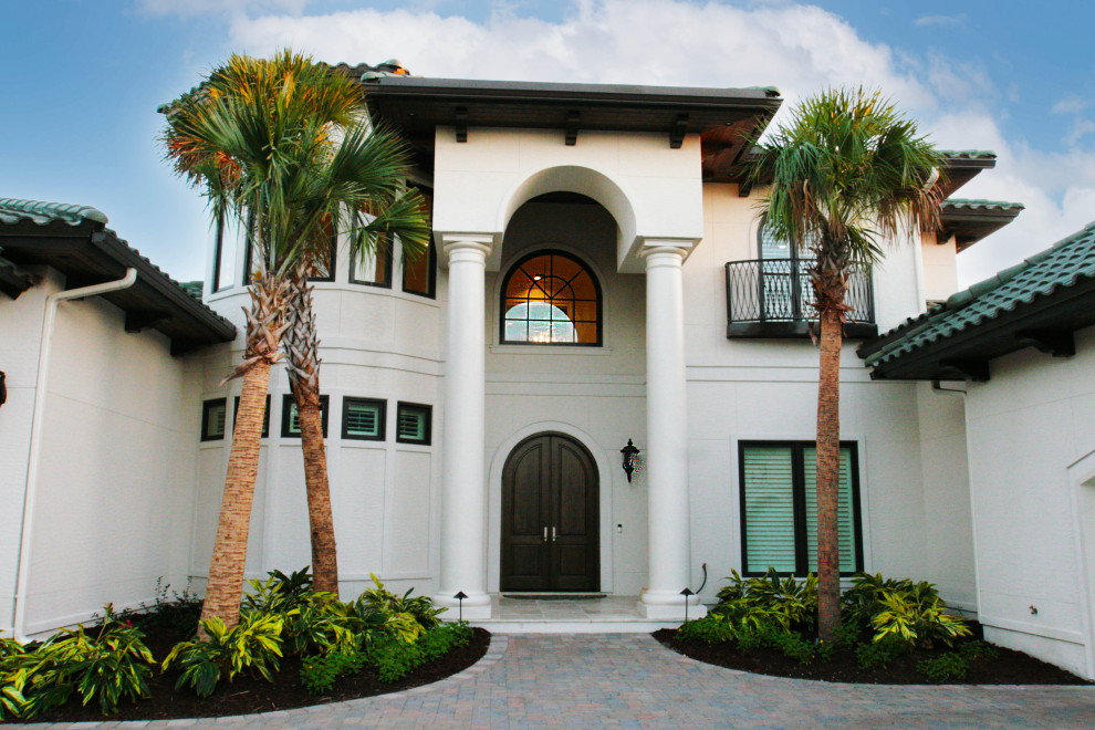 На фото: большой, двухэтажный, белый дом в средиземноморском стиле с облицовкой из цементной штукатурки и мансардной крышей с
