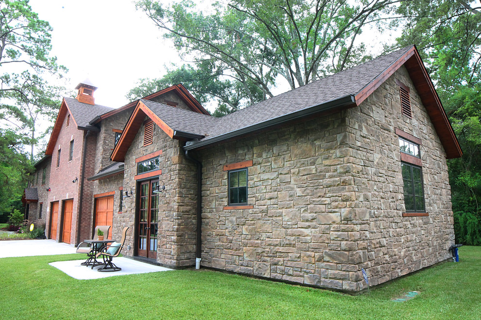 Esempio della facciata di una casa grande grigia country a due piani con rivestimento in pietra e tetto a capanna