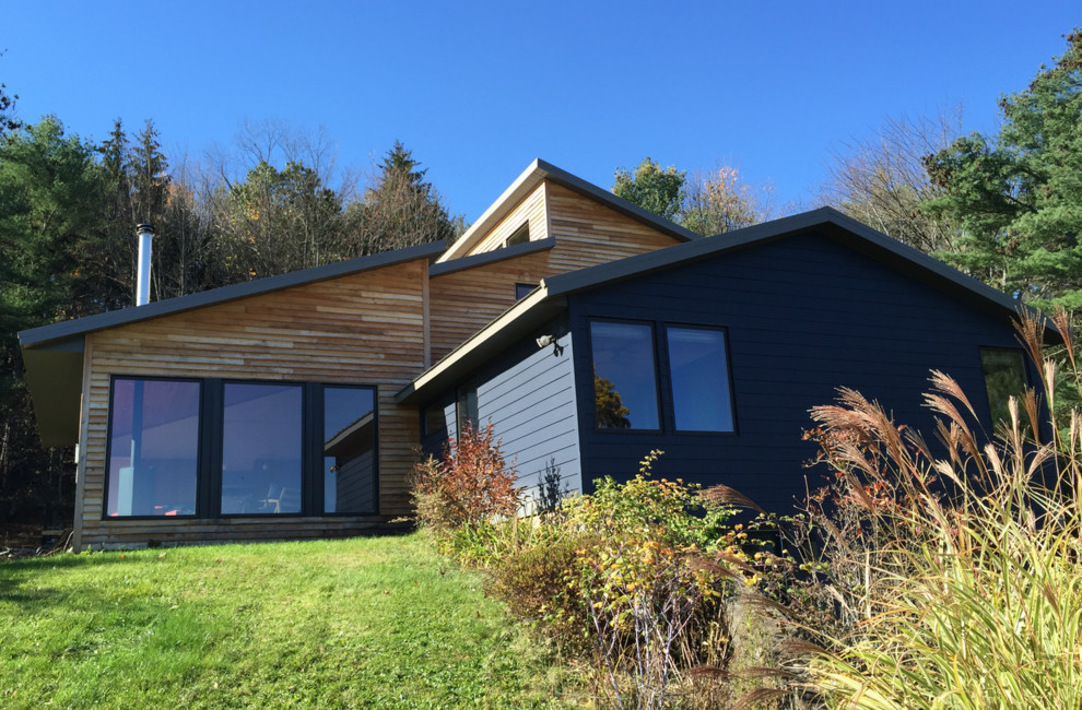 На фото: двухэтажный, деревянный, синий частный загородный дом среднего размера в стиле ретро с односкатной крышей и металлической крышей