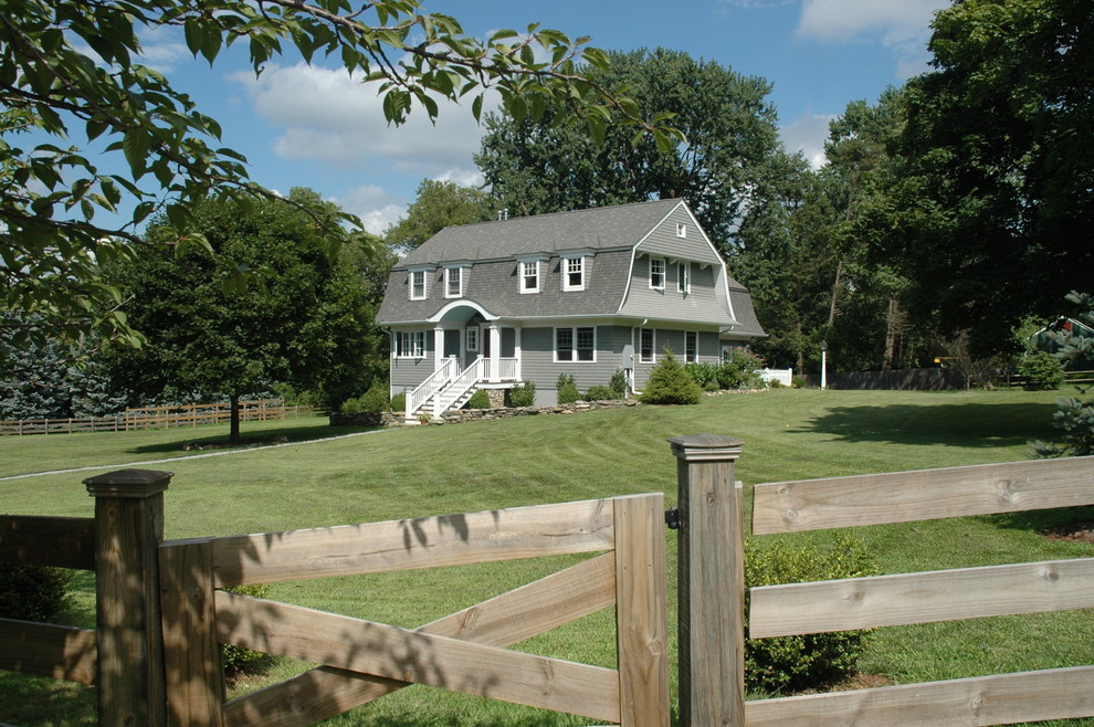 Esempio della facciata di una casa grigia country a due piani con rivestimento in legno e tetto a mansarda