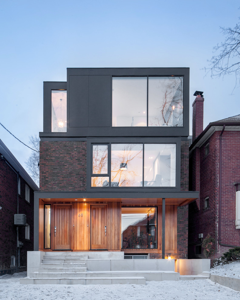 This is an example of a black contemporary house exterior in Toronto with three floors and a flat roof.